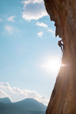 Rock climber climbing rock, man doing olympic sport on natural terrain, strength and endurance training, rock climber on the background of high mountains and blue sky