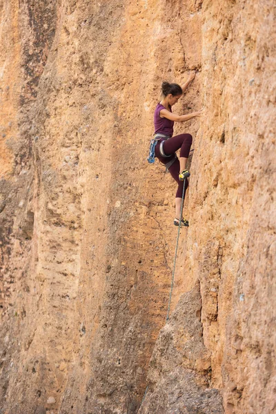 The girl climbs the rock. The climber is training to climb the rock. A strong athlete overcomes a difficult climbing route. Extreme hobby. A woman goes in for sports in nature. Natural rocky terrain