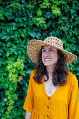 Şapkalı ve sarı elbiseli genç ve güzel bir kız kameraya gülümsüyor. Yakın plan. Tatildeki mutlu kız..