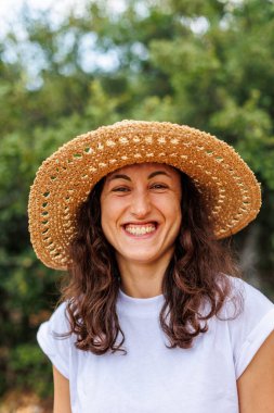 Hasır şapkalı güzel, mutlu bir kızın portresi. Kız gülümsüyor ve dışarıda eğlenmeyi seviyor. Yakın plan..