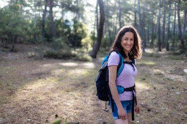 Sırt çantalı genç bir kız ormanda seyahat ediyor. Ormanda ve dağlarda turist yürüyüşü. Kız kameraya gülümsüyor. yürüyüş ve macera konsepti.