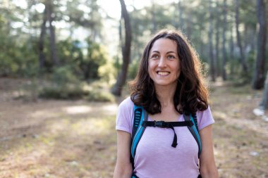 Sırt çantalı genç bir kız ormanda seyahat ediyor. Ormanda ve dağlarda turist yürüyüşü. Kız kameraya gülümsüyor. yürüyüş ve macera konsepti.
