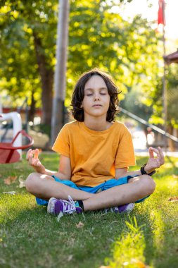 Çocuk parkta çimlerin üzerinde oturur ve meditasyon yapar. sakinlik ve konsantrasyon.
