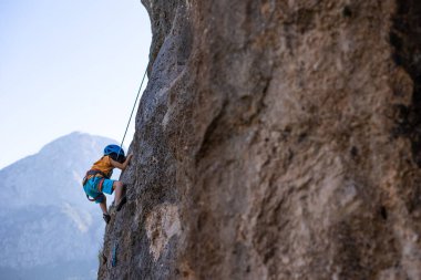 Çocuk kaya tırmanışı. Çocuk dağların arka planına karşı bir kayaya tırmandı. Olağanüstü bir hobi. Atletik bir çocuk güçlü olmayı öğrenir. Yükselen güvenlik.