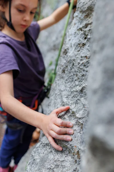 rock climber's hand close-up. child rock climber in a blue protective helmet overcomes the route in the mountains. children's sports in nature. active time in nature.