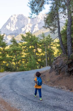 Sırt çantalı bir çocuk dağ yolunda gider. Çocuk gezisi. Çocuklarla hafta sonu.