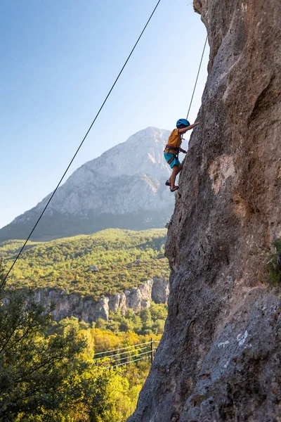 Children's rock climbing. The boy climbs a rock against the backdrop of mountains. Extreme hobby. An athletic child trains to be strong. Climbing safety.