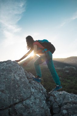 Sırt çantalı bir kadın dağa tırmanır, dağlarda yürüyüş yapar, hedefe ulaşmada başarı elde eder, gün batımında bir dağın arka planına karşı bir kızın silueti