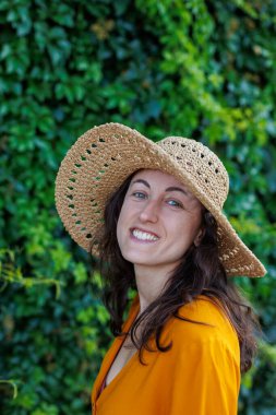 Şapkalı ve sarı elbiseli genç ve güzel bir kız kameraya gülümsüyor. Yakın plan. Tatildeki mutlu kız..