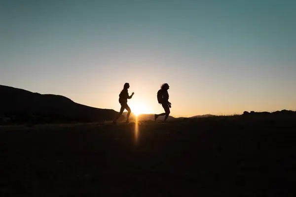 Running people over rough terrain. two girls train outdoors in a beautiful mountain landscape at sunset. silhouette of two girls during a hike in the mountains.