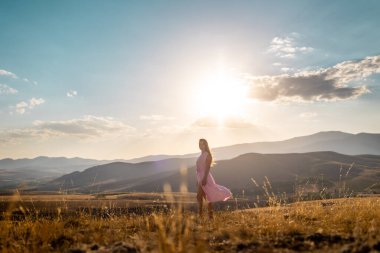 girl walks against the backdrop of the mountains. a young girl in a pink dress enjoys a walk in the mountains.
