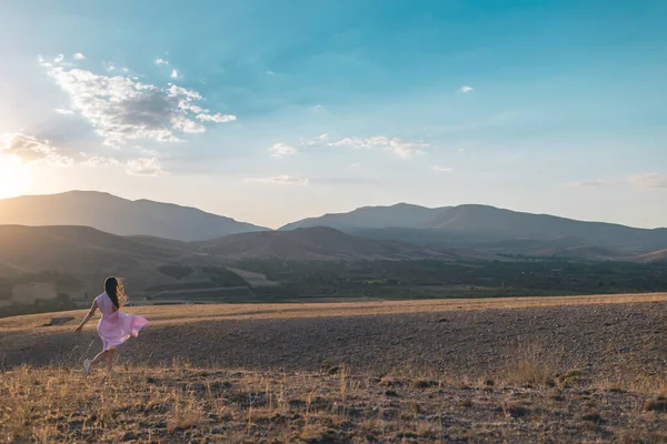 girl walks against the backdrop of the mountains. a young girl in a pink dress enjoys a walk in the mountains.