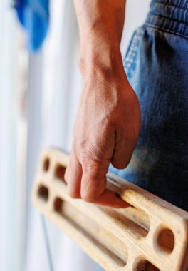 Kaya tırmanışçısının güçlü erkek eli, parmak eğitimi için bir tahta tutuyor. Evde tırmanma egzersizi. Kaya tırmanışçısının eli yakın çekim. Güç ve dayanıklılık. klavye ve askı