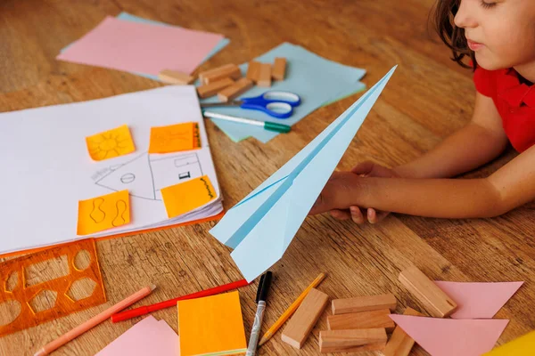 子供は紙から飛行機のモデルを作ります 少年は ハサミと紙と婚約してる 子供は自宅で創造に携わっています 子供はパイロットになることを夢見ています — ストック写真