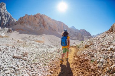 Çocuk sırt çantasıyla dağlarda geziyor. Yüksek dağlarda dağ yürüyüşü. Çocuk bir dağ yolunda yürüyor. Türkiye.