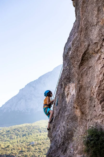 儿童攀岩 那男孩在高山的背景下爬上一块岩石 极端的嗜好一个运动的孩子训练得很强壮 攀爬安全 — 图库照片