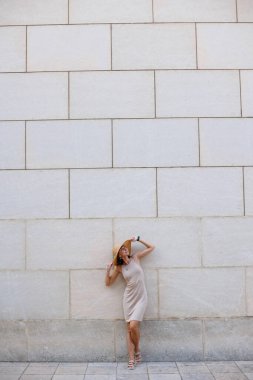 Yazlık elbisesi ve şapkası ile sokakta duvarın yanında poz veren güzel bir kız. Seksi kaygısız kadın dışarıda eğleniyor..
