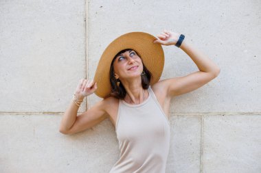 Yazlık elbisesi ve şapkası ile sokakta duvarın yanında poz veren güzel bir kız. Seksi kaygısız kadın dışarıda eğleniyor..