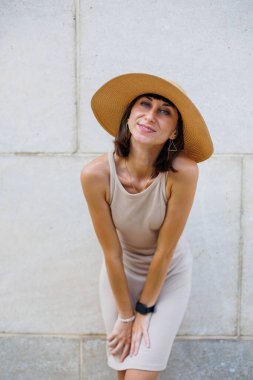 Moda bir yaz elbisesi içinde gülümseyen güzel bir kız. Sokakta şapkalı, duvara karşı poz veren seksi kaygısız kadın. Eğlence ve kahkaha.