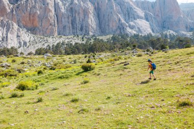 Çocuk gezisi. Arka planda kayalık dağlar olan sırt çantalı bir çocuk gezgin. Yaz tatili ve yürüyüş yaşam tarzı kavramı