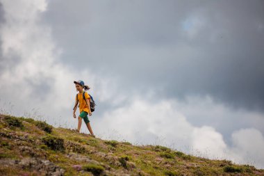 Çocuk sırt çantasıyla dağlardaki bulutların arkasına gidiyor. Sırt çantalı çocuk gezgini, yürüyüş, seyahat, yaşam tarzı konsepti