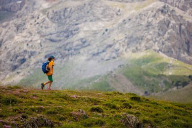 Sırt çantalı bir çocuk dağların arka planında yürüyüş yapıyor. Sırt çantalı çocuk gezgini, yürüyüş, seyahat, yaşam tarzı konsepti, arka planda dağlar, yaz tatili çocukları..