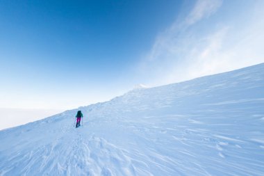 Bir kadın karda kar ayakkabılarıyla yürür, kış yürüyüşü yapar, kışın dağlarda yürüyüş malzemesi taşır.