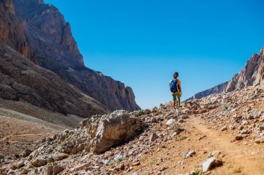 Sırt çantalı küçük bir çocuk dağın arka planına karşı yol boyunca ayakta duruyor. Seyahat ve yürüyüş. Çocuklarla dağlara git. Hindi. Aladaglar.