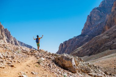 Sırt çantalı küçük bir çocuk dağın arka planına karşı yol boyunca ayakta duruyor. Seyahat ve yürüyüş. Çocuklarla dağlara git. Hindi. Aladaglar.