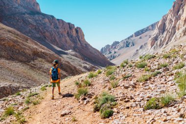 Çocuk sırt çantasıyla dağlarda geziyor. Yüksek dağlarda dağ yürüyüşü. Çocuk bir dağ yolunda yürüyor. Türkiye.