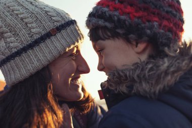 Anne ve oğul sarılıp birbirlerine bakıyorlar. Mutlu anne ve oğulun portresi. Sokakta kış yürüyüşü.