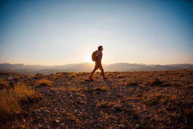 Yalnız geziye. Sırt çantalı bir adam dağların arka planında yol boyunca yürür. Sırt çantasıyla dağlarda yürüyüş. Yürüyüş ve seyahat kavramı.