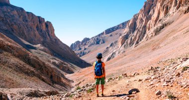 Sırt çantalı küçük bir çocuk dağın arka planına karşı yol boyunca ayakta duruyor. Seyahat ve yürüyüş. Çocuklarla dağlara git. Hindi. Aladaglar.