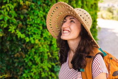 Yeşil bir duvarın arkasında sırt çantalı ve şapkalı genç bir kızın portresi. Yaz tatili. tatil ve macera konsepti.