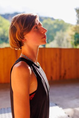 Zayıf, sarışın bir kadın fitness paspasına oturur, vücudunu açık havada gerer, fotokopi alanı ile panorama yapar. Açık hava idman konsepti