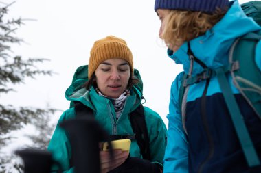 Kış yürüyüşü sırasında açık havada iki çekici bayan yürüyüşçünün portresi. Yürüyüş sırasında iki turist telefonu kullanıyor.