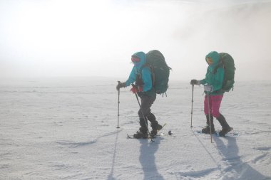 Kar fırtınası sırasında kar ayakkabıları ve sırt çantalı iki kız karda yürür. dağcılık