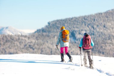 Two women with backpacks walk in snowshoes in the snow, winter trekking, two people in the mountains in winter, hiking equipment. winter holiday