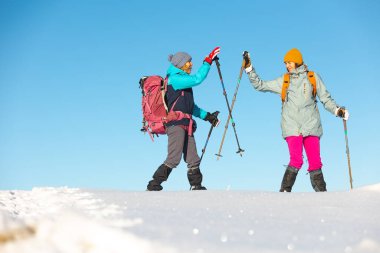 İki kadın karda kar ayakkabılarıyla yürüyor, kış yürüyüşü yapıyor, kışın dağlarda iki kişi yürüyüş ekipmanları, beşlik çakıyor.