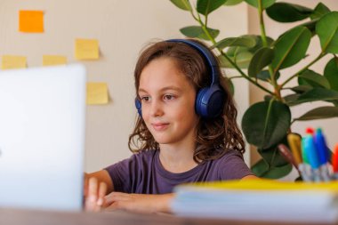 Çocuk derste müzik dinler. Kıvırcık saçlı çocuk mesafeli öğrenme ile mutlu. Dersler İnternet üzerinden yapılıyor.