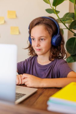 Çocuk derste müzik dinler. Kıvırcık saçlı çocuk mesafeli öğrenme ile mutlu. Dersler İnternet üzerinden yapılıyor.