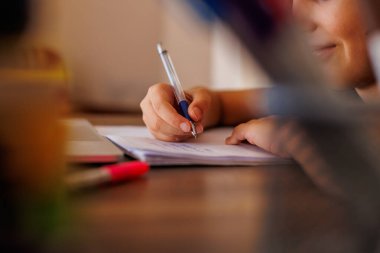 Evde masasında otururken ödevini yaparken yazmayı öğrenen odaklanmış küçük bir çocuğun yan görüntüsü. Yazmayı öğrenen zeki bir anaokulu öğrencisinin portresi.. 
