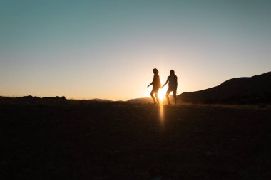 Gün batımında dağlarda seyahat ederken sırt çantalı iki kızın silueti. Gün batımında iki kişi dağ sıraları boyunca yürür. Özgürce seyahat et..