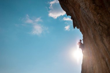 Rock climber climbing rock, man doing olympic sport on natural terrain, strength and endurance training, rock climber on the background of high mountains and blue sky