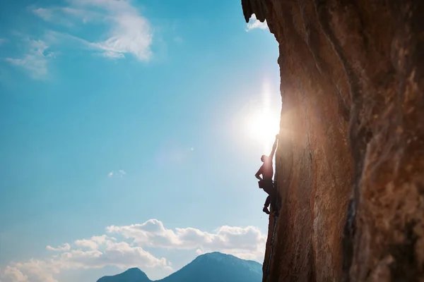 Kaya tırmanışçısı kaya tırmanışı, olimpiyat sporu yapan adam doğal arazi, güç ve dayanıklılık eğitimi, yüksek dağların arka planında kaya tırmanıcısı ve mavi gökyüzü.