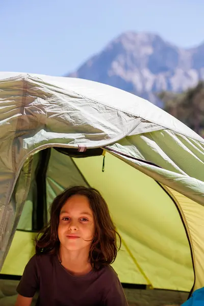Aile tatili ve seyahat. Neşeli çocuk çadırda oturuyor. Çocuklarla seyahat etmek. Ormanda yürüyüş yapmak ve çadırda yaşamak. macera ve tatil kavramı.