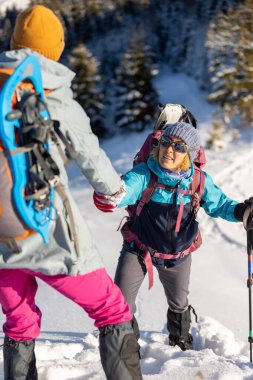 Takım arkadaşının tırmanmasına yardım eden dağcı, sırt çantalı bir kadın arkadaşına yardım elini uzattı, kışın yürüyüşe çıkan iki kız.