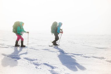 Turistler kışın dağlarda birlikte seyahat ederler. İki kız, karla kaplı dağlar. Dağlarda kar ayakkabılarıyla yürüyüş yapmak.