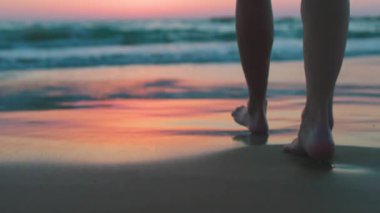 Gün batımında kumsalda çıplak ayakla yürüyen bir kadının ayak izleri, kumda ayak izleri ve suda yansımalar. Sakinlik ve sükunet. Yaz tatilindeki turist