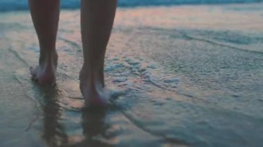 Gün batımında kumsalda çıplak ayakla yürüyen bir kadının ayak izleri, kumda ayak izleri ve suda yansımalar. Sakinlik ve sükunet. Yaz tatilindeki turist